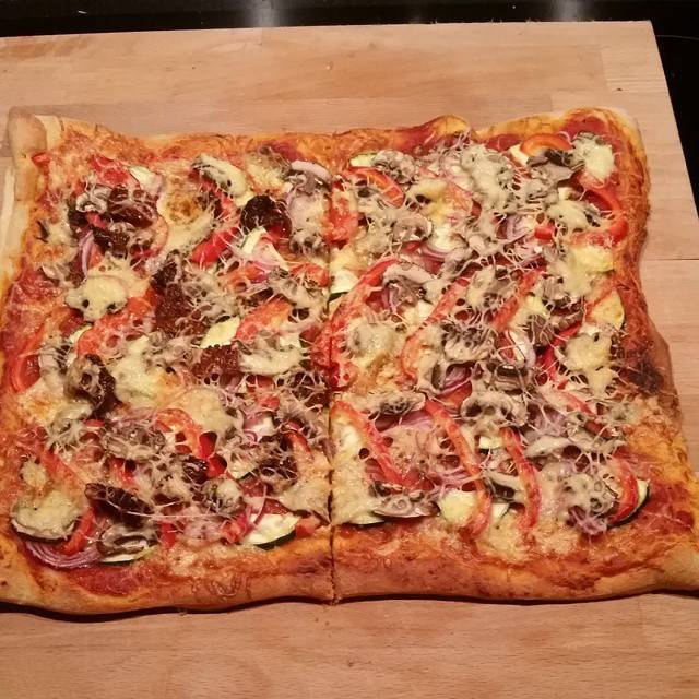 A homemade flatbread pizza topped with tomato, cheese and red onion, on a wooden board.