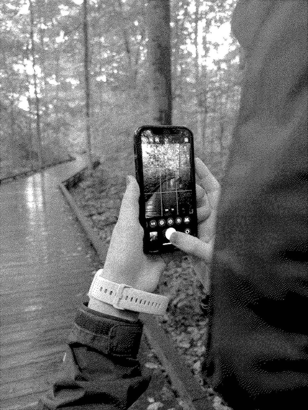 black and white dithered photo of a person pressing the shutter button in the iOS camera app