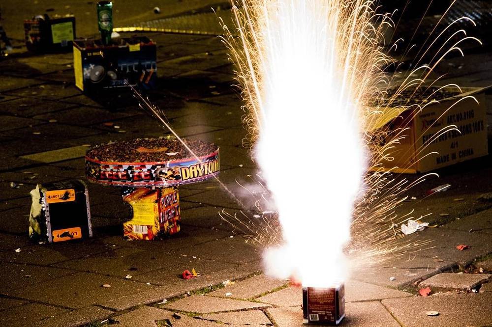 A firework shooting sparks upward from a device on a city street at night.