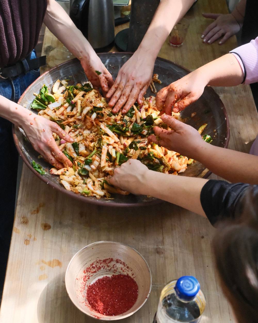Group of people making kimchi in a traditional bowl
