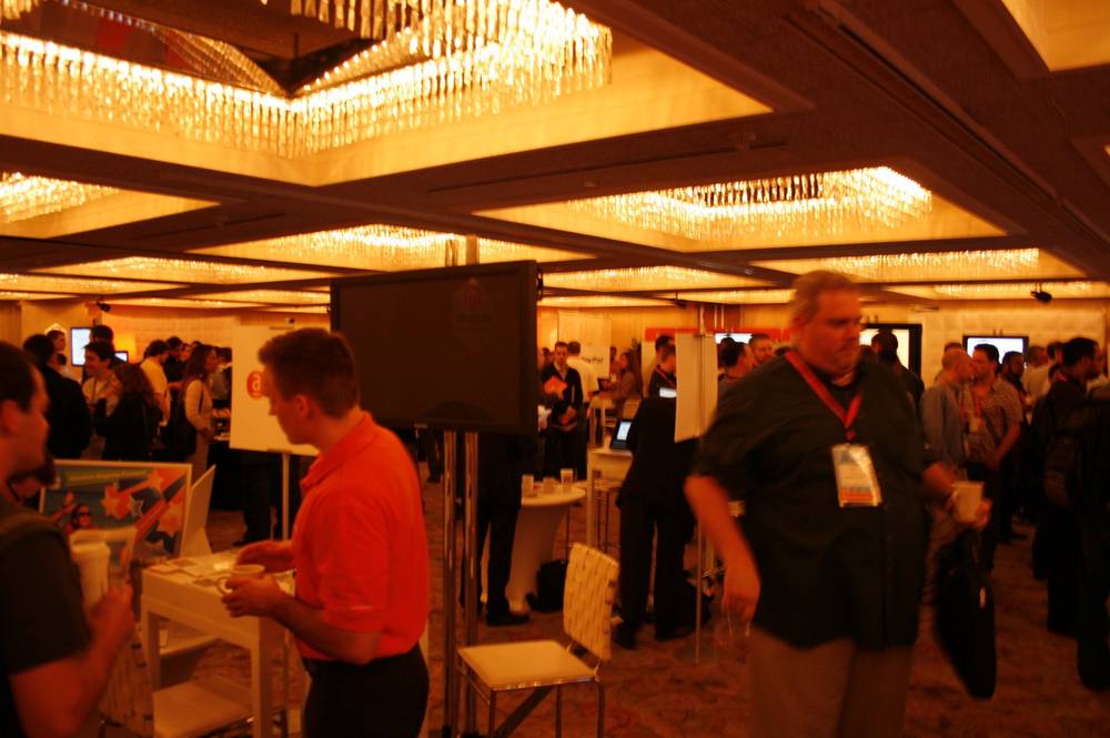 Attendees in orange shirts and lanyards mingle at a busy conference expo booth.