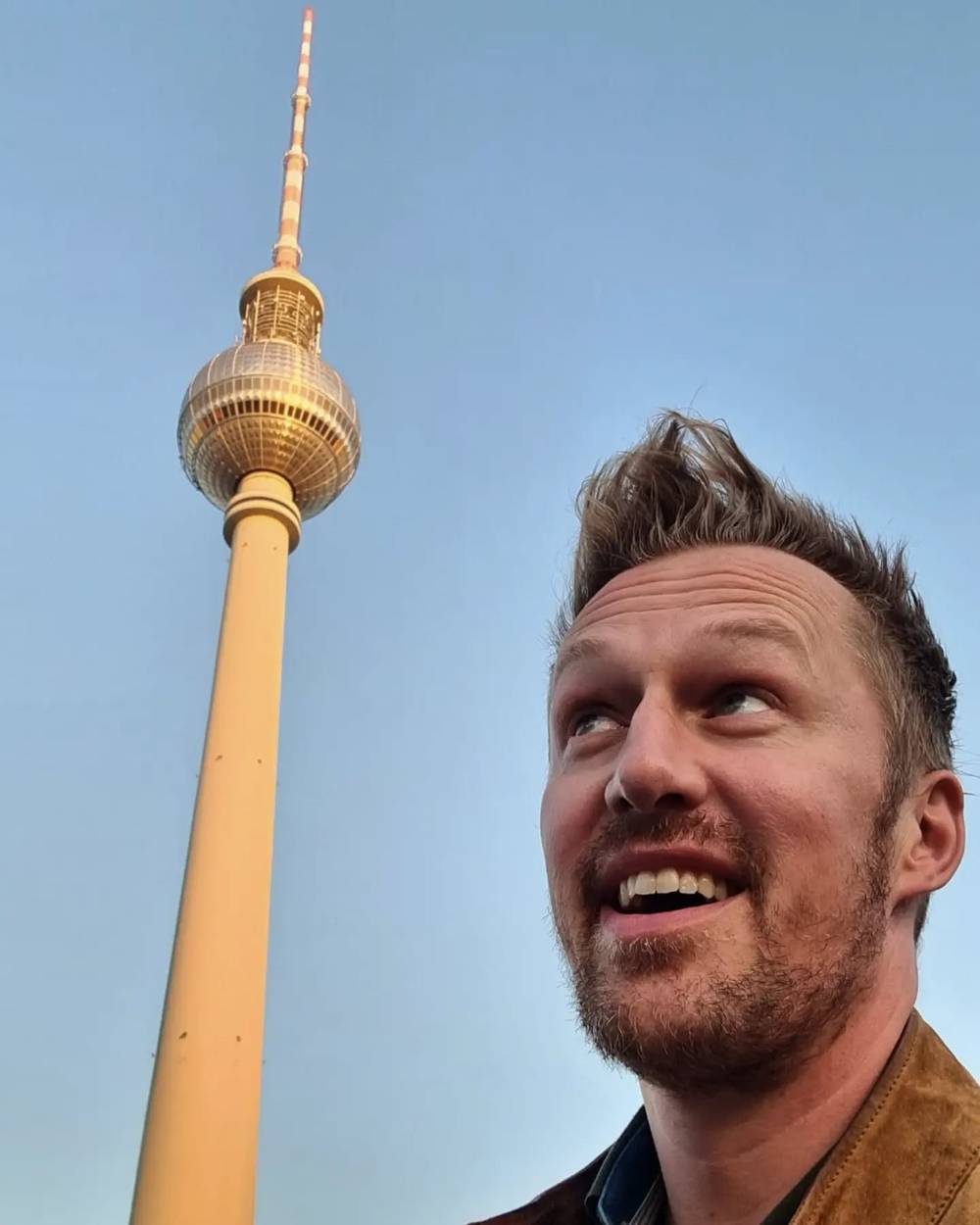 Guido looking up and smiling beneath the Berlin TV Tower against a clear blue sky.