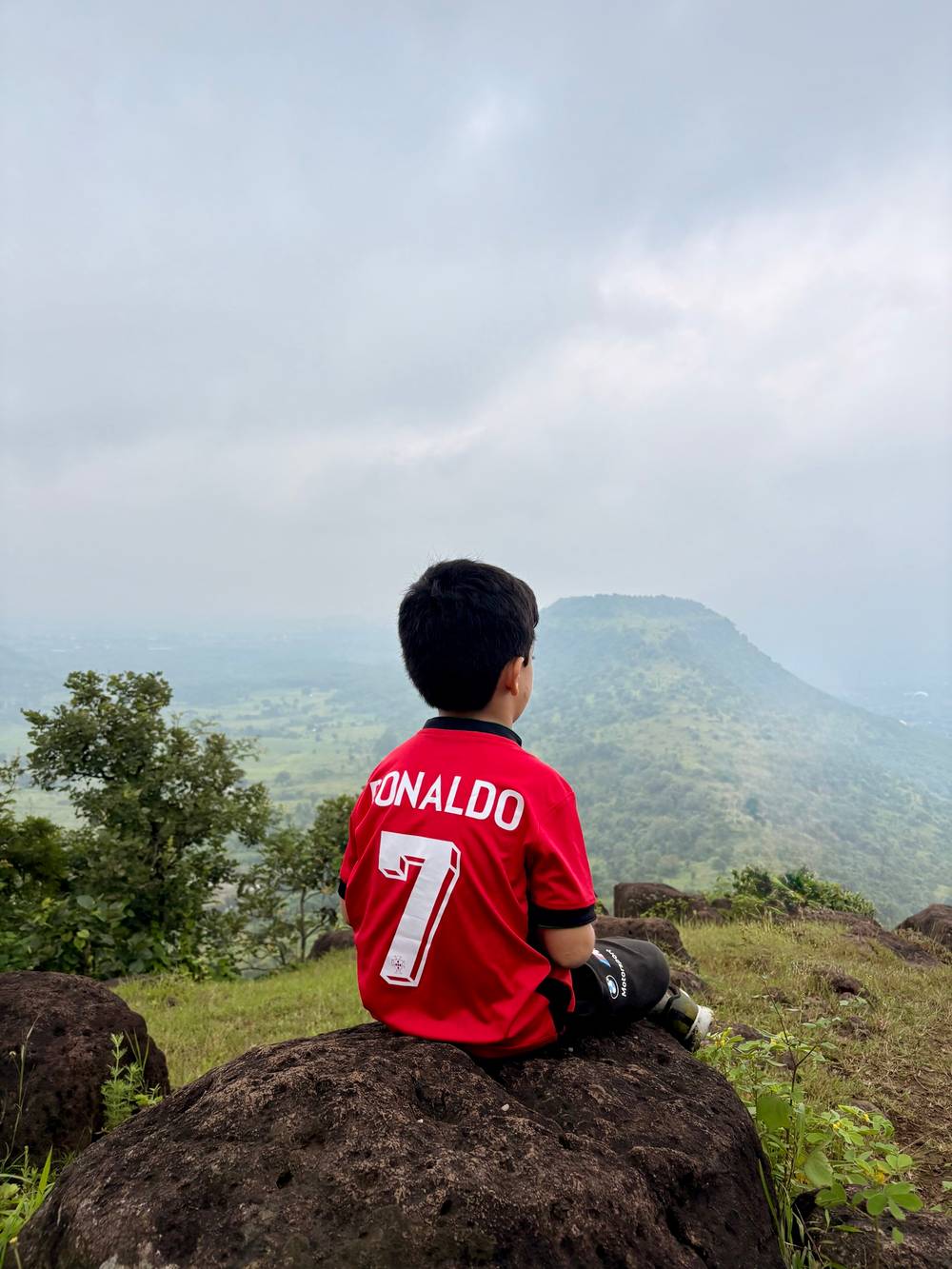 A boy wearing a Ronaldo jersey against a backdrop of lush green hills