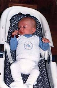 A newborn baby lies in a bouncer chair wearing a white onesie.