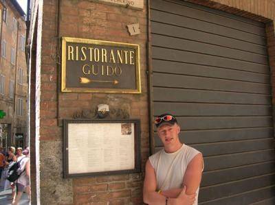 A man poses grinning beside a restaurant sign reading 'Ristorante Guido'.