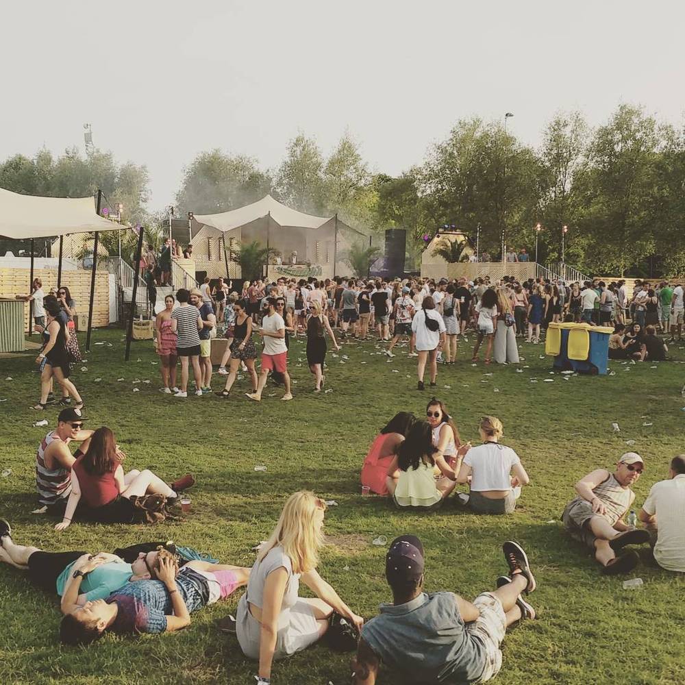 People sitting and lying on the grass at an outdoor festival on a hazy day.