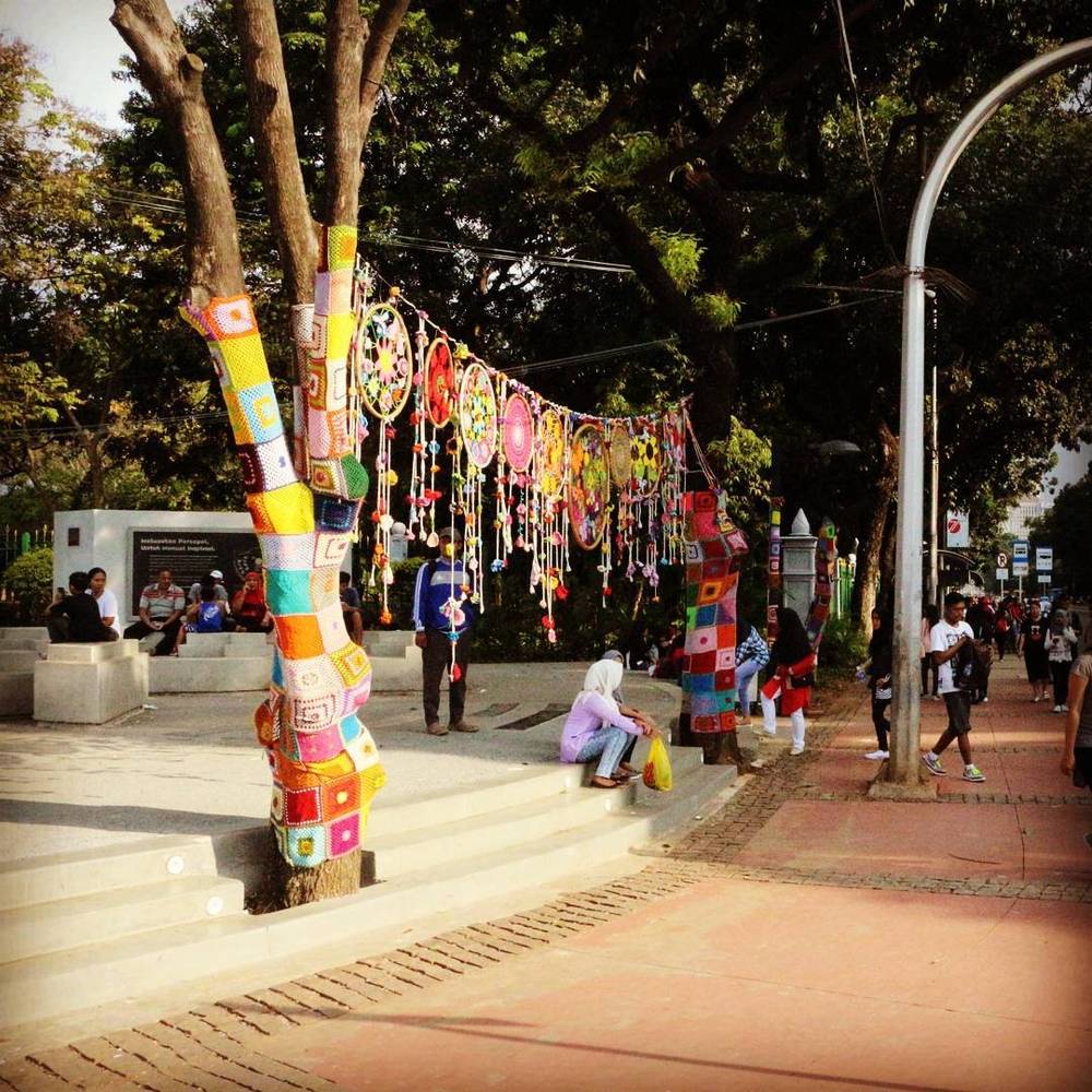 A tree wrapped in colourful yarn bombing decorations in a park.