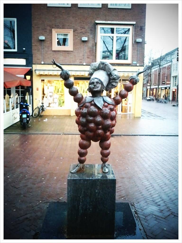 A bronze statue of a cherry-covered figure with arms raised stands in a town square.