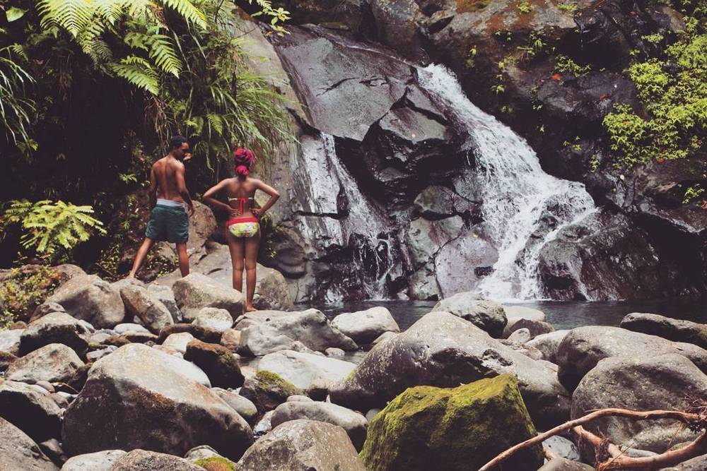 Two people standing on rocks looking at a waterfall in a forest.