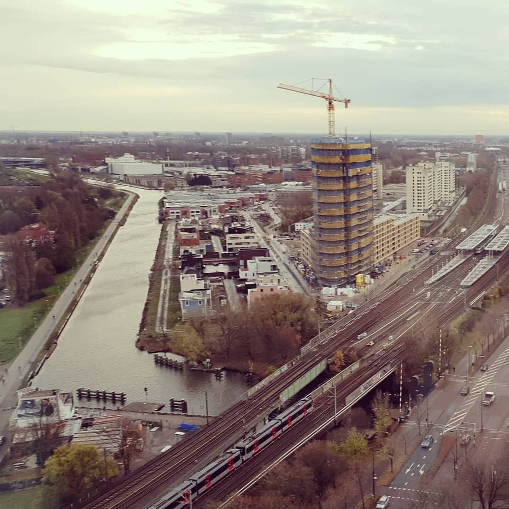 Aerial view of a river and railway bridge with a tower under construction in the distance.