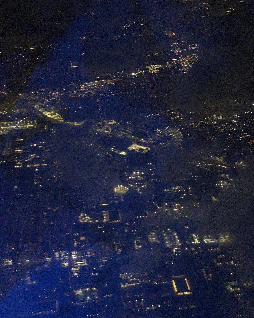 A grainy dark, but colorful photo of the city of Houston visible through sporadic brakes in the clouds.