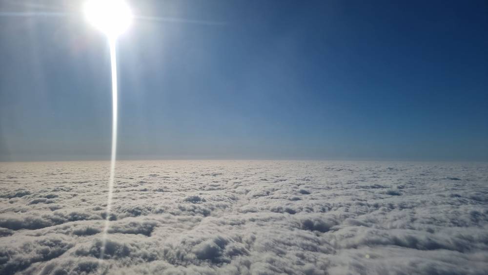 A shaft of sunlight through clouds, seen from an airplane window.