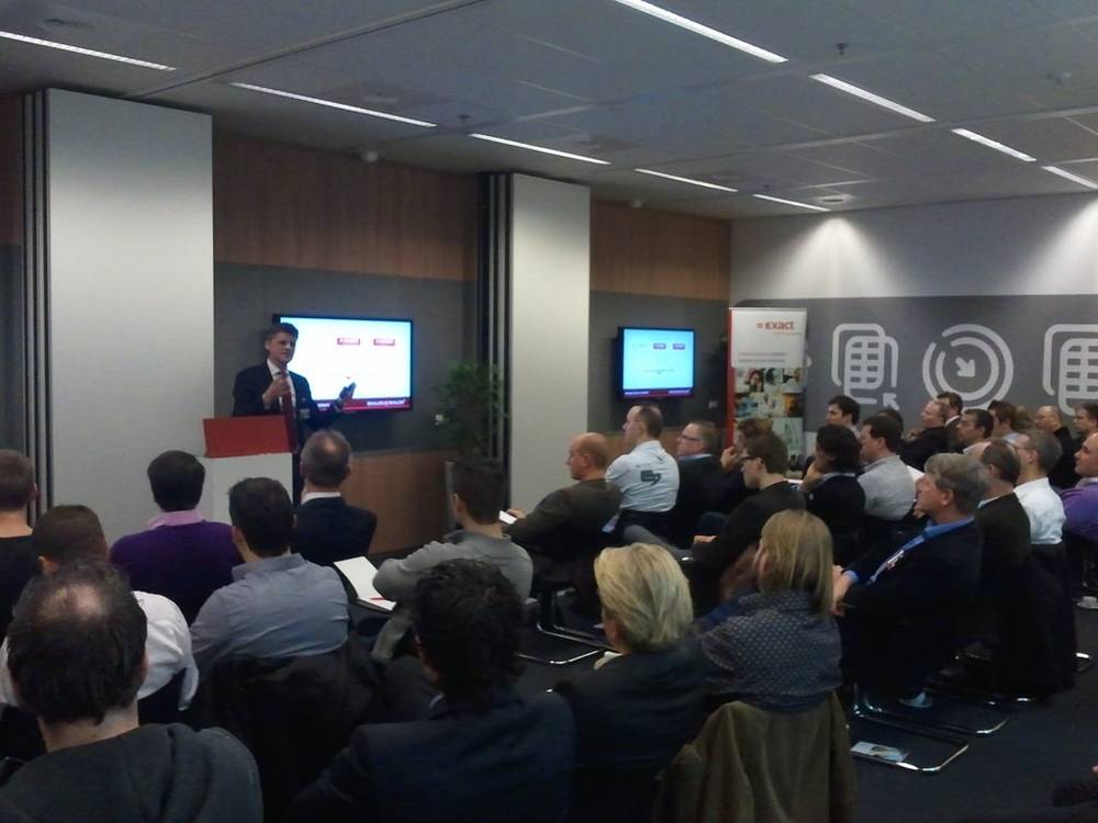 A packed room of more than fifty people listens to a presentation at Exact.