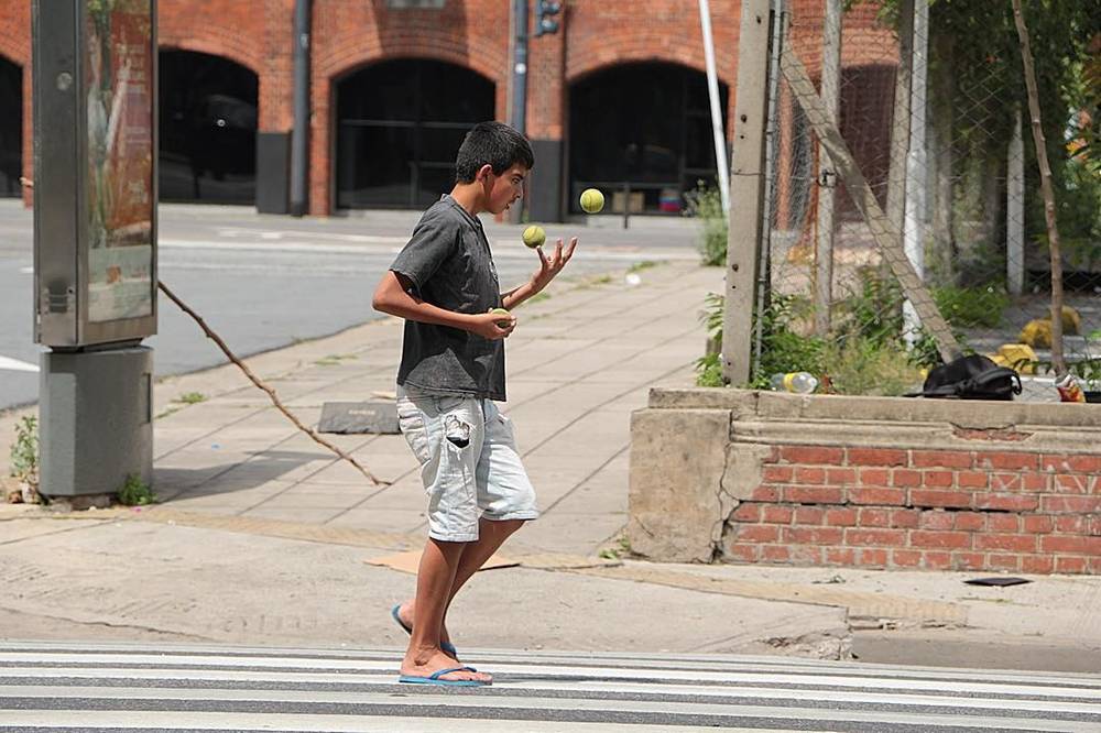 A man juggling on a street crossing near an old brick warehouse building.