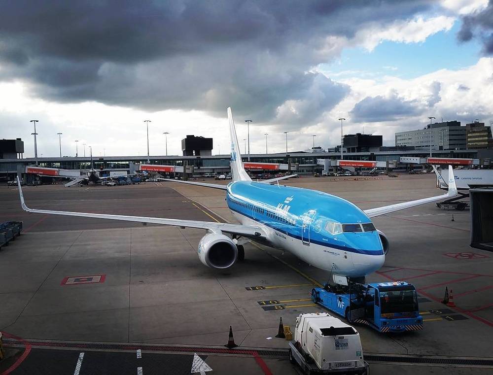 A KLM passenger plane parked on the tarmac under a dramatic cloudy sky.