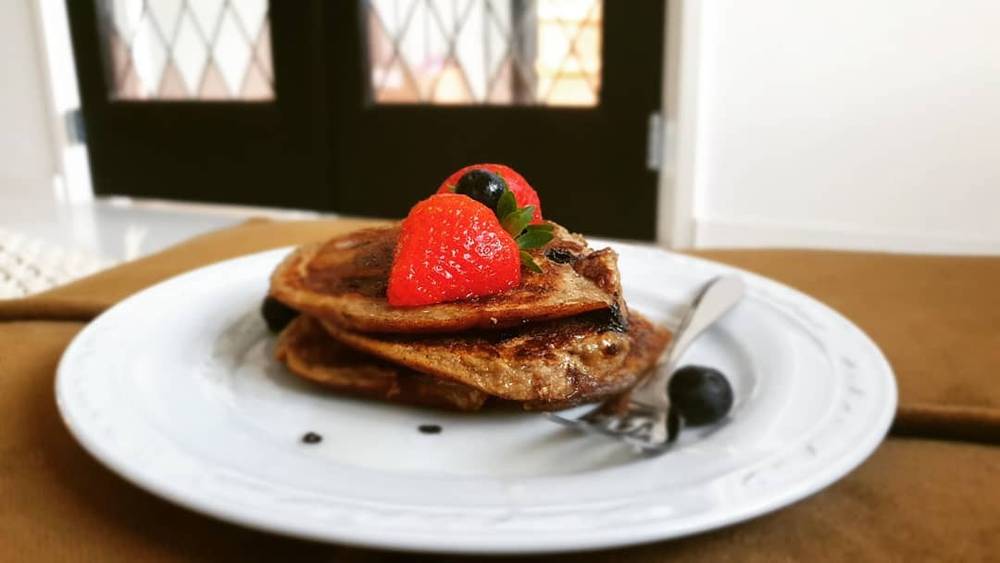 A plate of pancakes topped with a strawberry and berries.