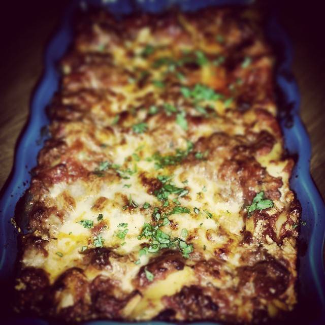 Close-up of a baked casserole dish topped with melted cheese and herbs.