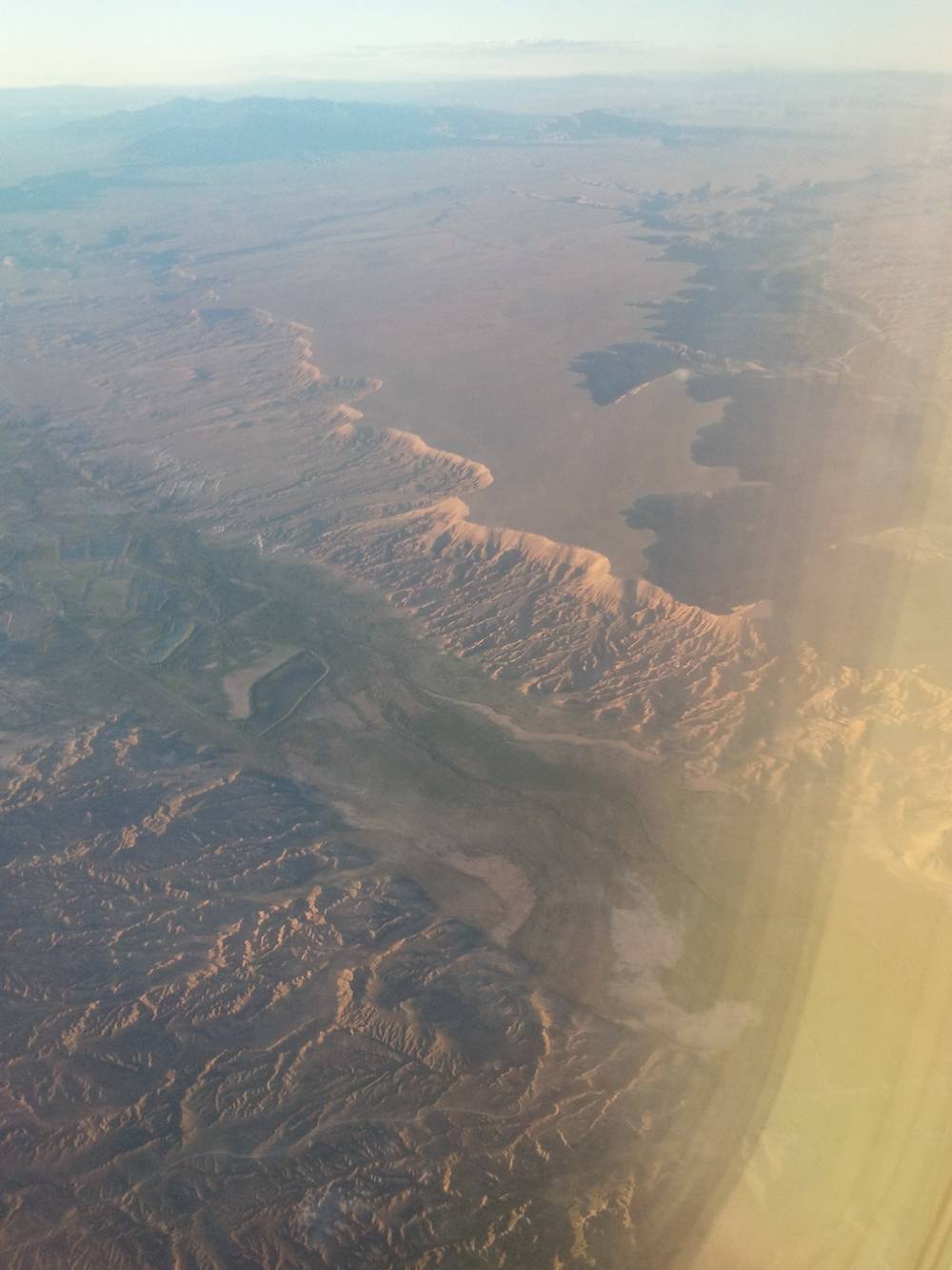 Aerial view of reddish canyon ridges and desert terrain from the plane window.