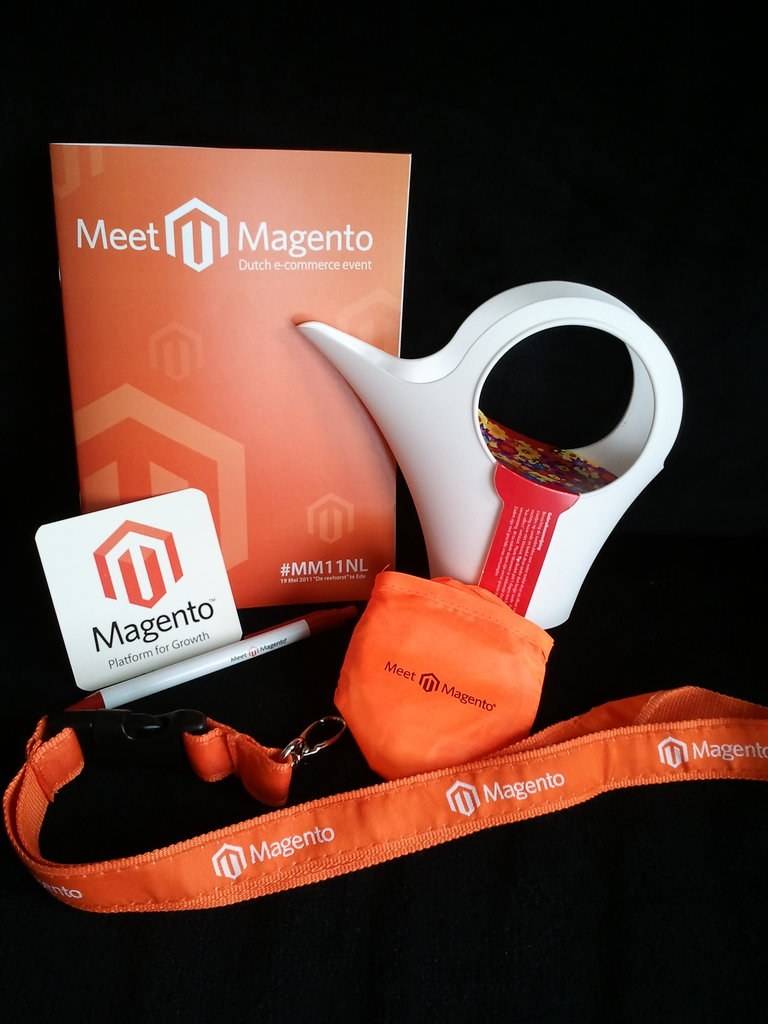 Meet Magento conference goodies, including a badge, bottle opener and small bag, laid out.