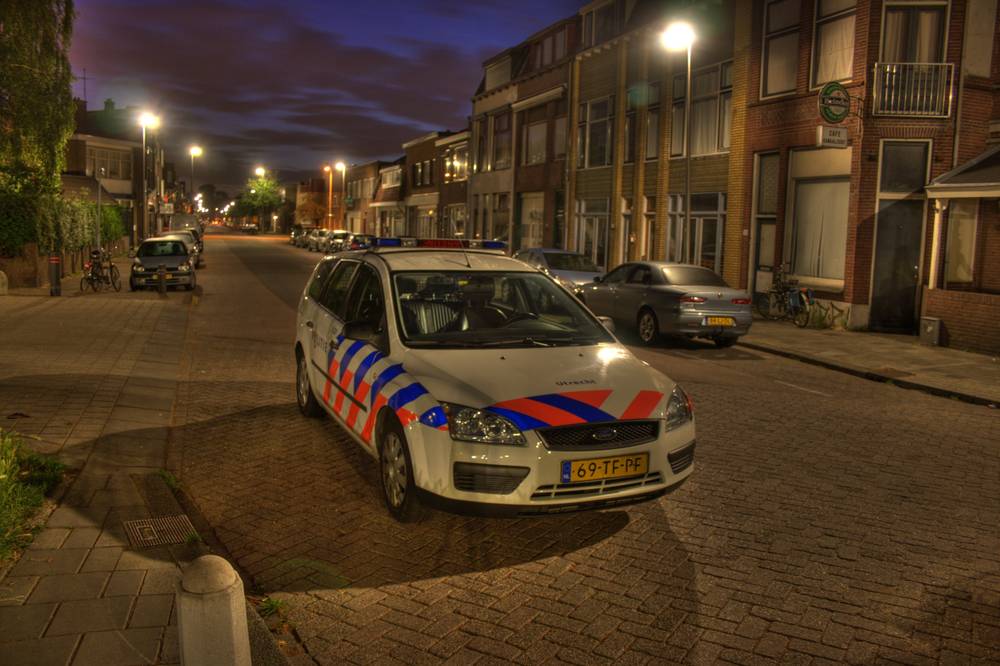 A Dutch police car parked on an empty cobblestone street at night.