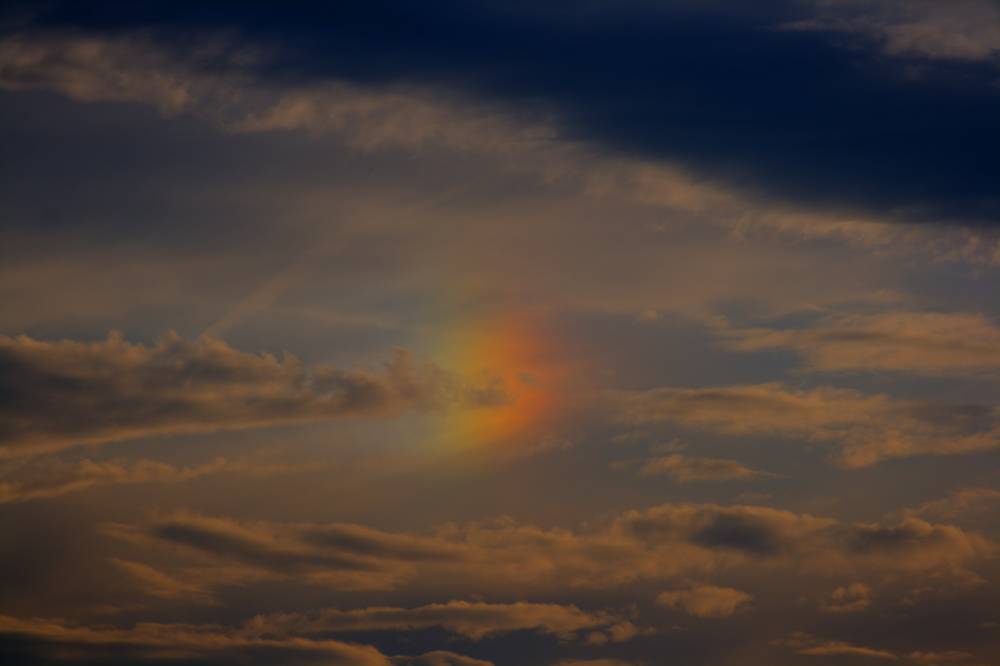 A close-up of a glowing sun dog halo in orange clouds at sunset.
