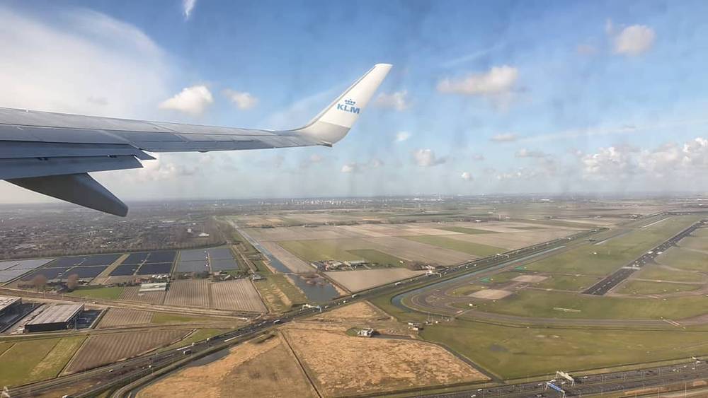 View from an airplane wing over farmland and a runway on a KLM flight.