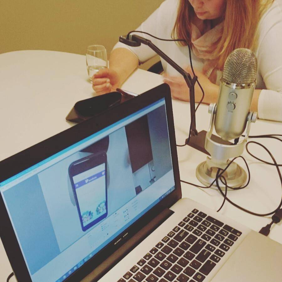 A person sitting at a desk with a laptop and microphone, holding a glass of wine.