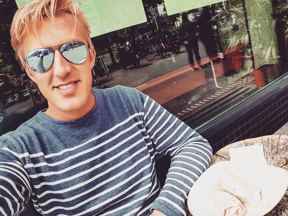 Selfie of a man in a striped shirt and sunglasses at an outdoor table.