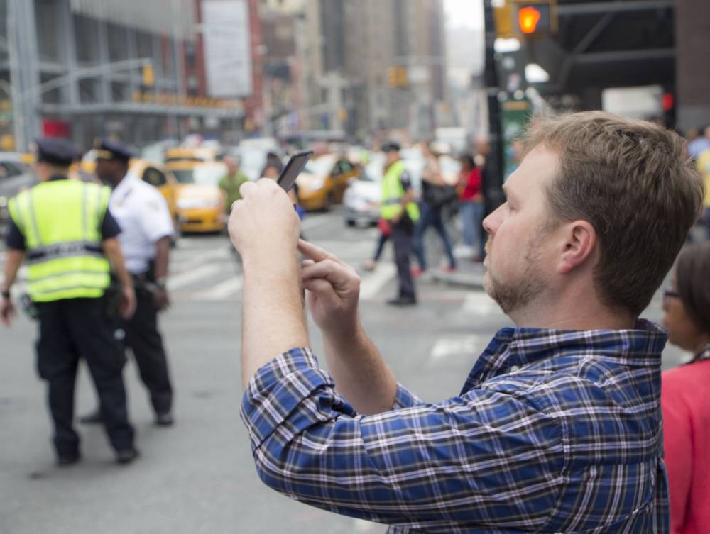 A man photographs a police-lined Times Square street with his phone.