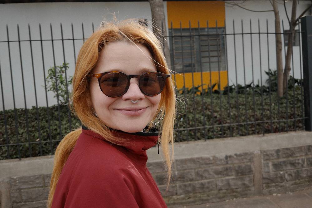 Bruna olhando pra câmera enquanto passeamos na rua. Ela usa óculos escuros.