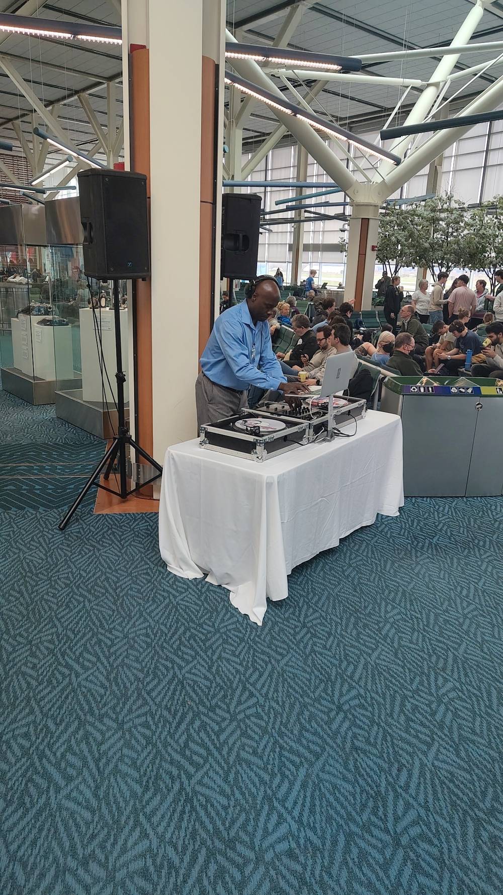 A DJ performs at a table during an event with a seated audience nearby.