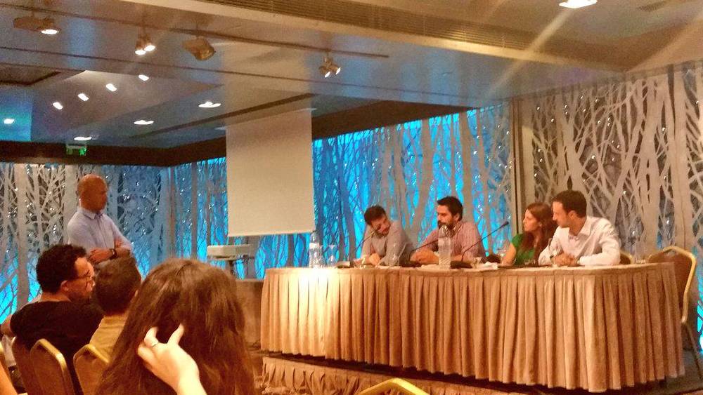 A panel discussion on stage with four speakers seated at a table in a conference room.