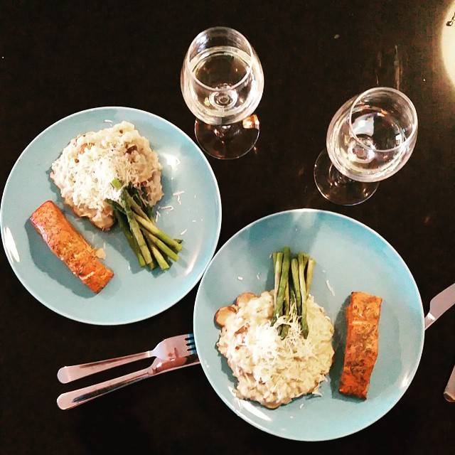 Two plates of salmon with asparagus and rice, seen from above with wine glasses on a dark table.