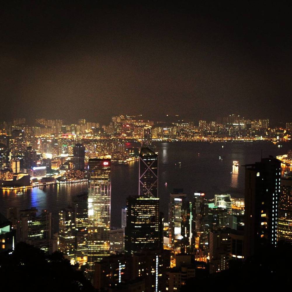 An aerial night view of a dense city skyline lit up along a harbor.