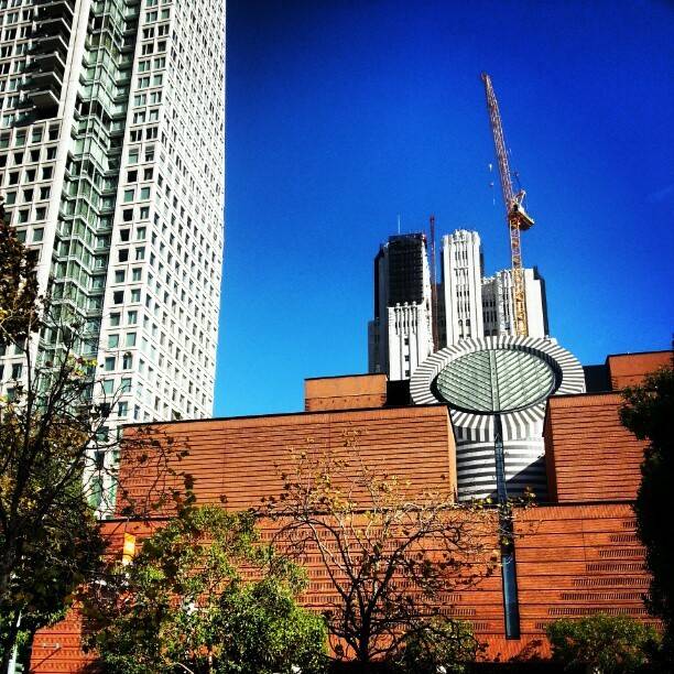 A modern high-rise building with a construction crane against a clear blue sky.