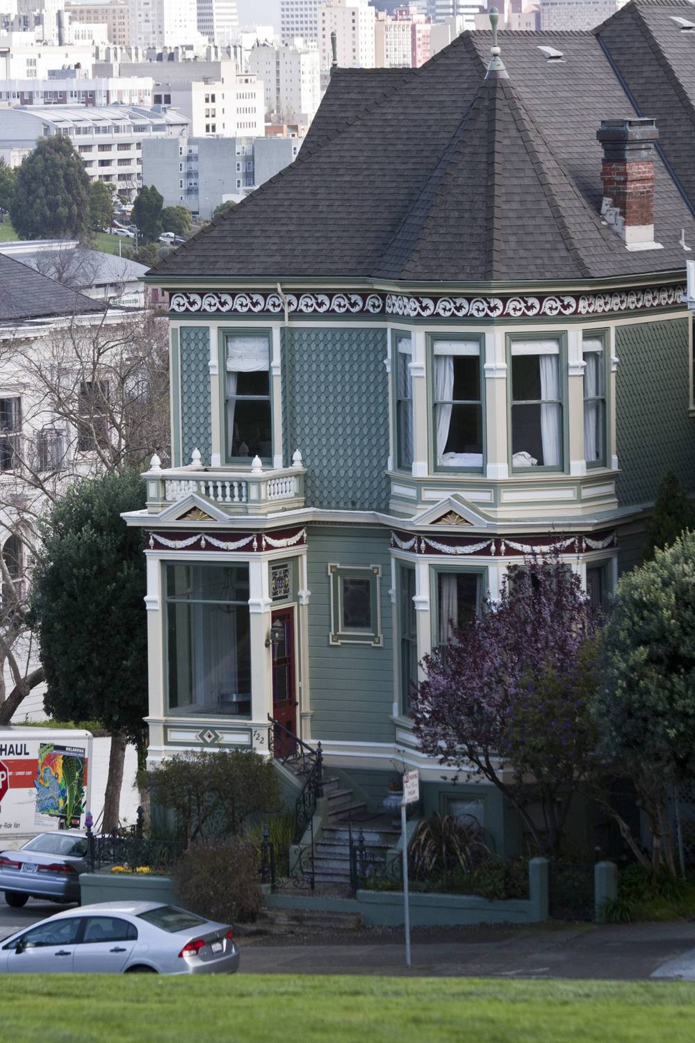 A green and white Victorian house with ornate trim sits on a corner lot.