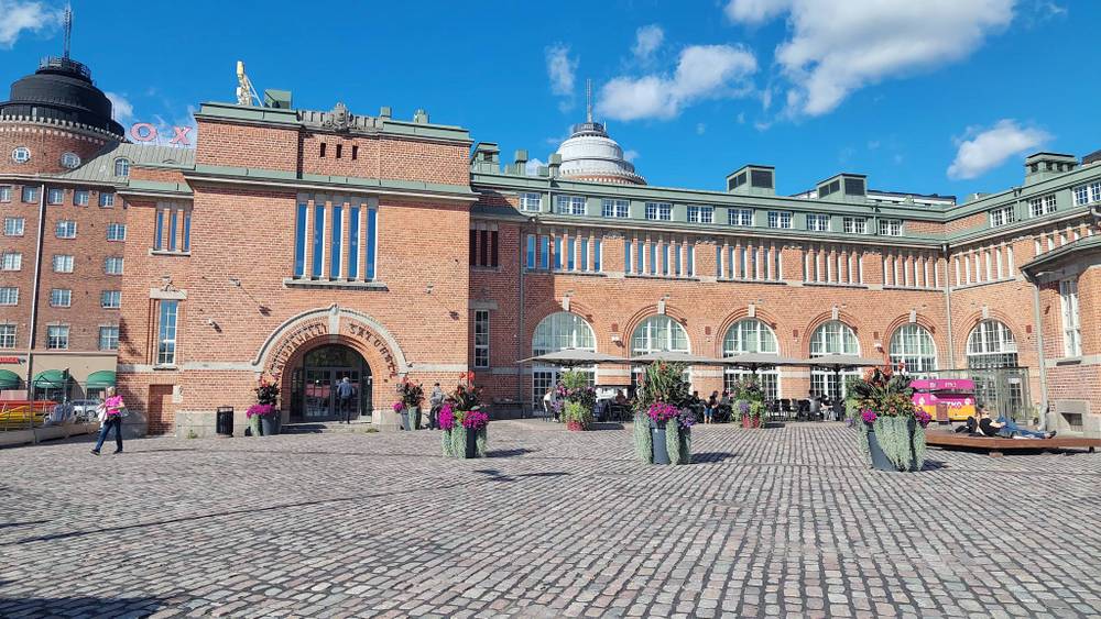 A red-brick market hall building with a domed tower on a cobblestone square.