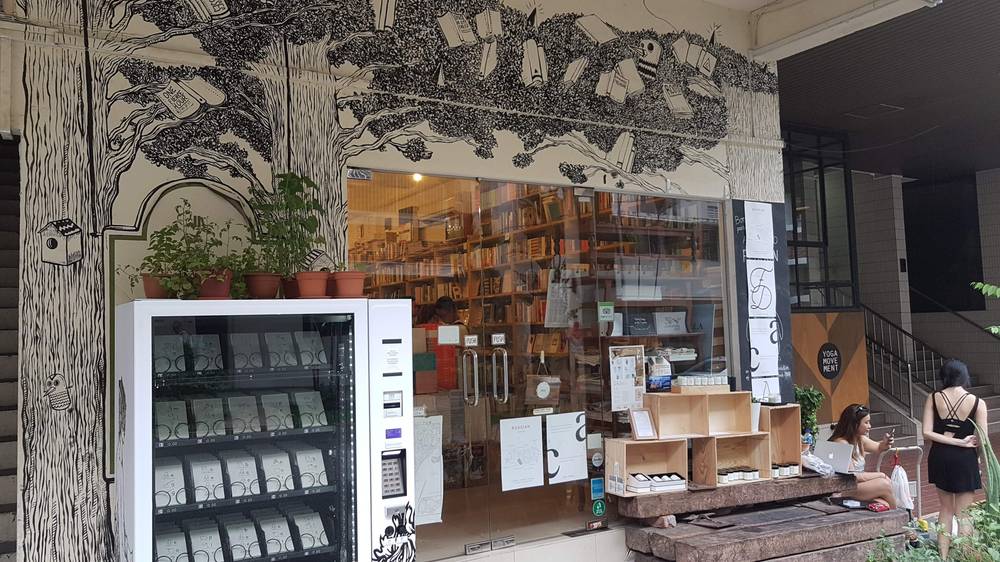 A bookstore storefront with an illustrated tree mural above the window and a vending machine outside.