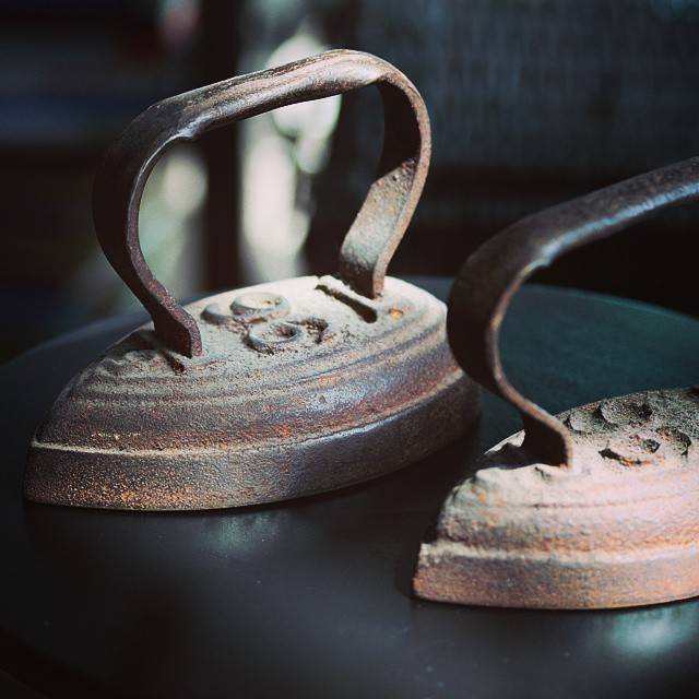 Two antique cast-iron flat irons resting on a dark surface.