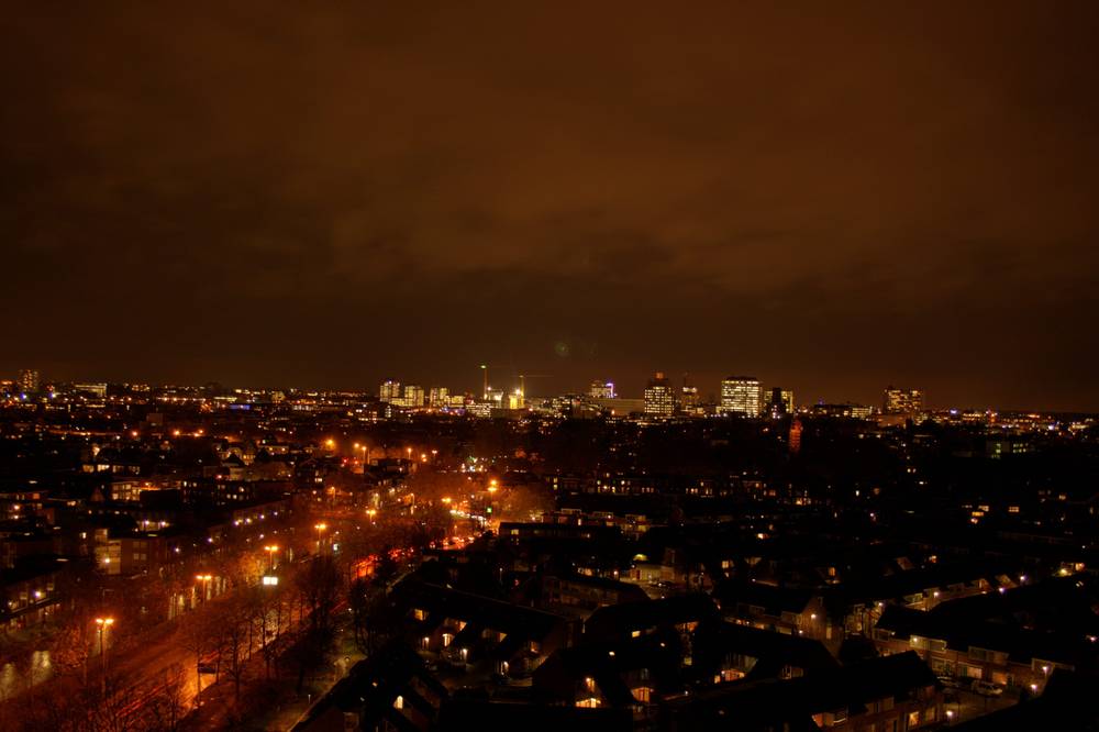 A wide night view of the Utrecht skyline with illuminated high-rise towers above a dark residential area.
