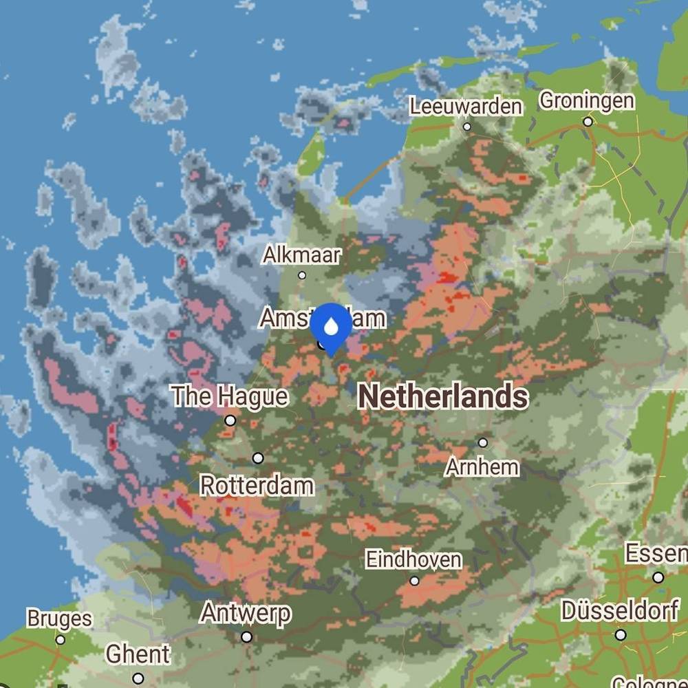 A weather radar map of the Netherlands showing scattered rain over Amsterdam and surrounding areas.