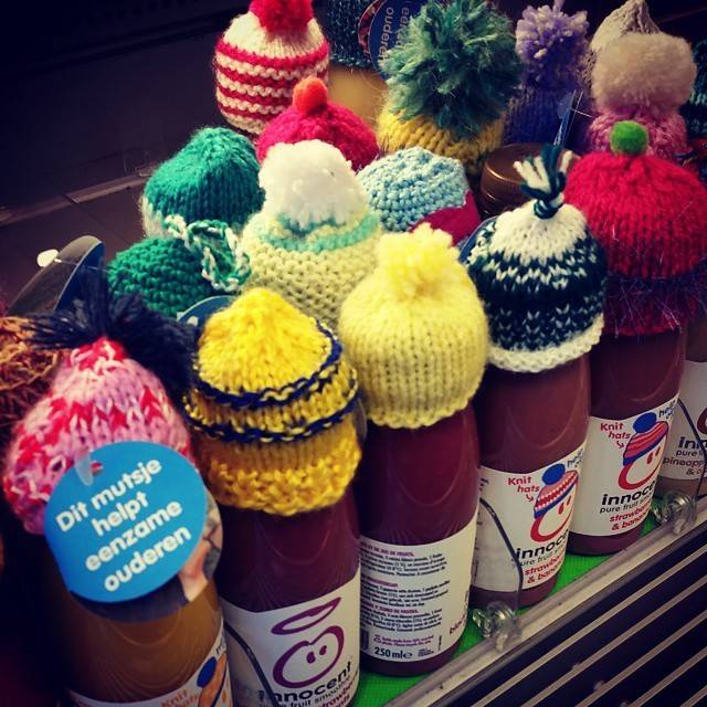 Colorful hand-knitted mini hats placed on bottles of Innocent smoothie, with a sticker reading 'Dit mutsje helpt eenzame ouderen'.