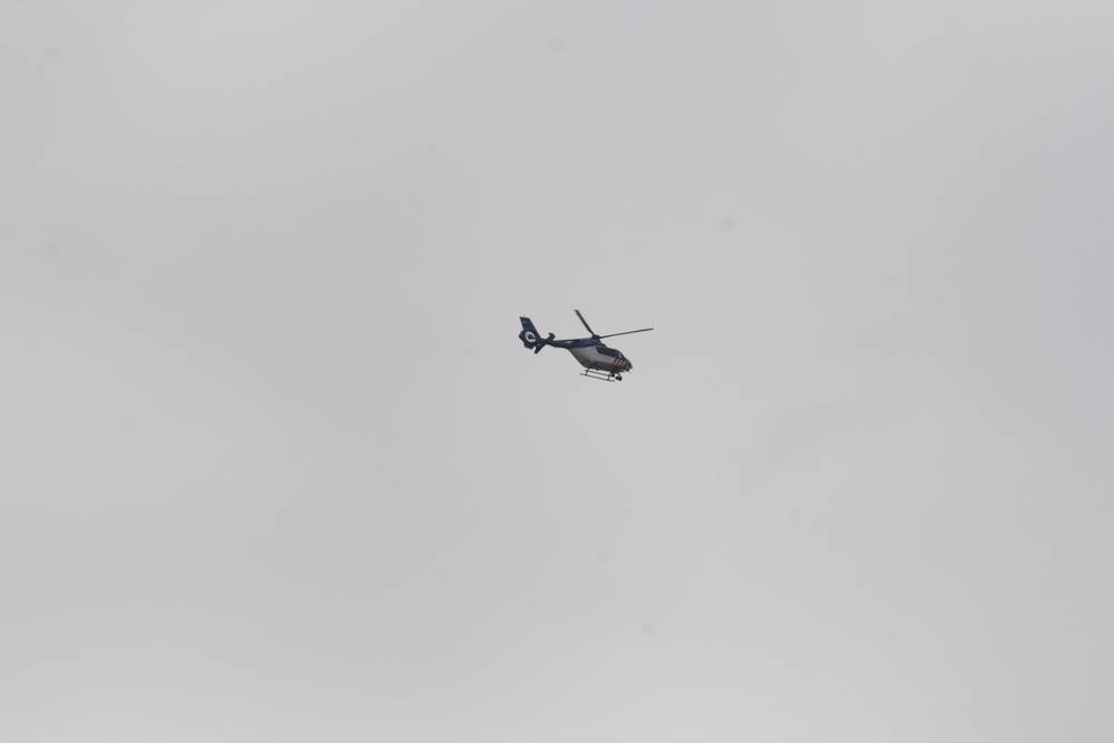A helicopter flies distantly in a hazy overcast sky above the race route.