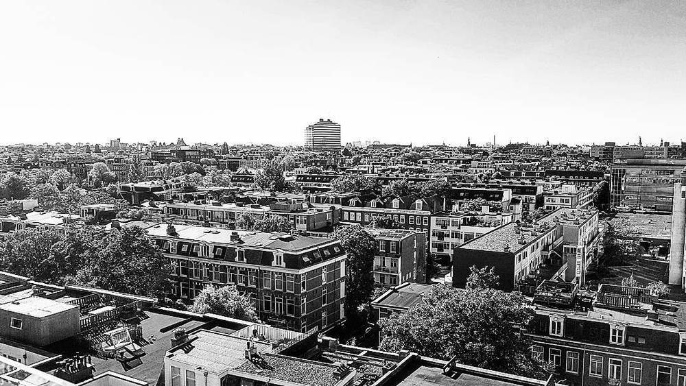 Black and white panoramic view over a dense city of rooftops and buildings.