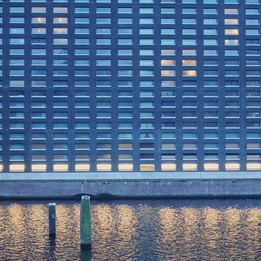 A modern building facade with rows of lit windows reflected in water.