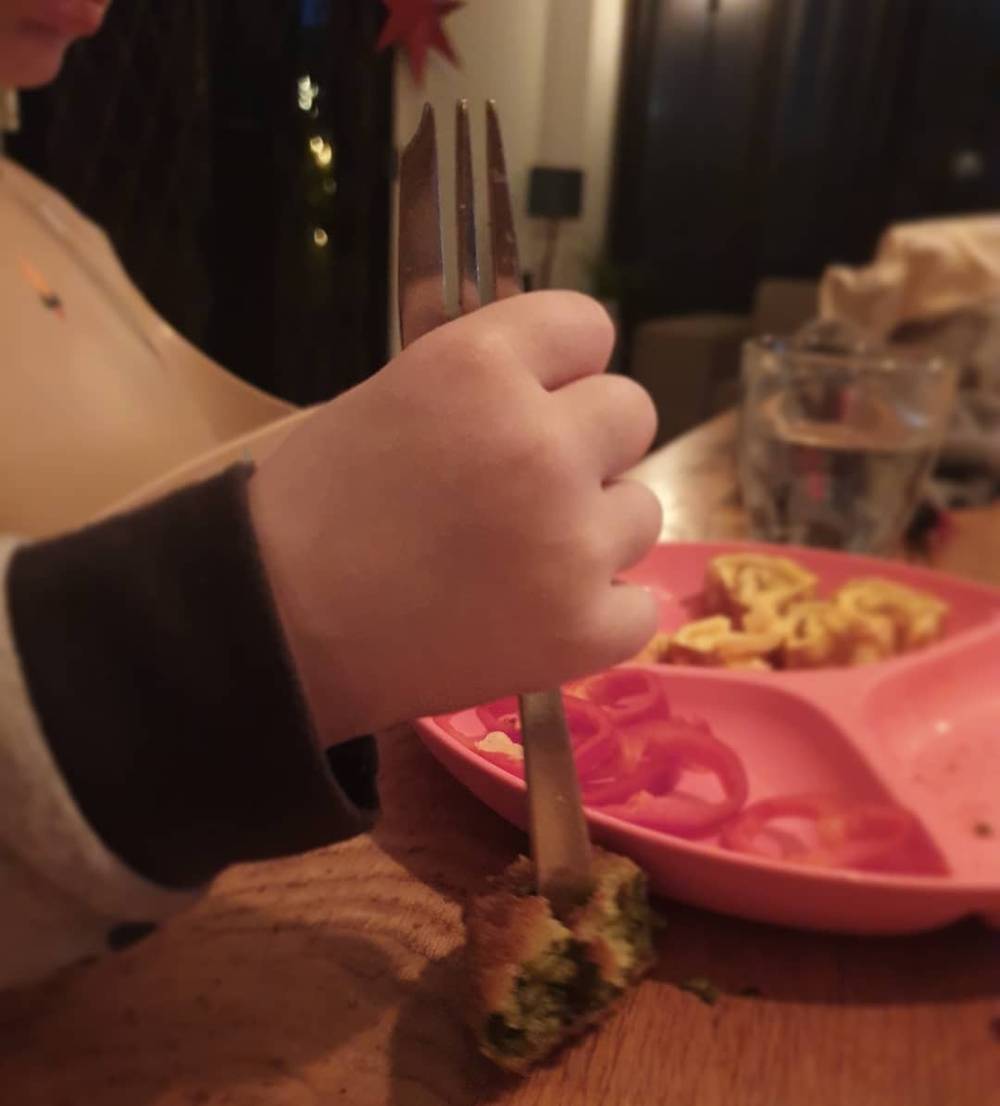 Close-up of a child's hand using a fork to eat from a pink divided plate.