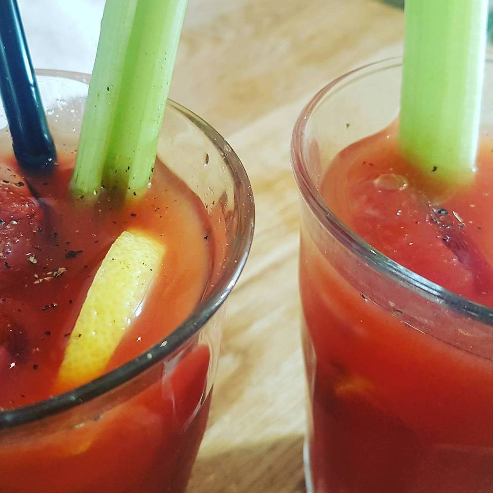 Two Bloody Mary cocktails garnished with celery stalks and lemon wedges.