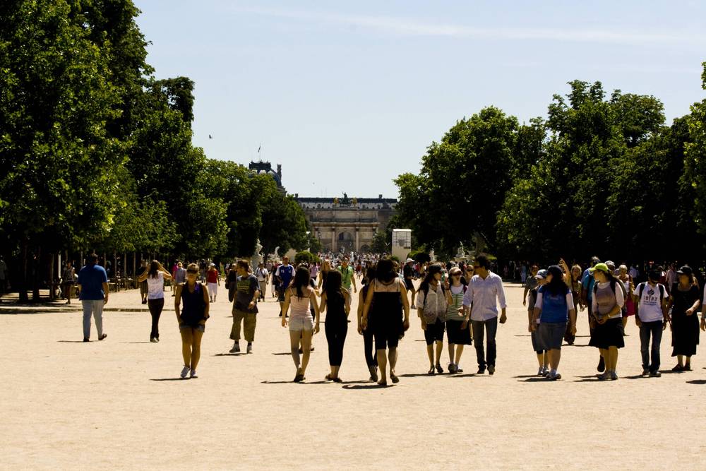 People walk along a wide gravel path lined with trees in the Tuileries Garden.