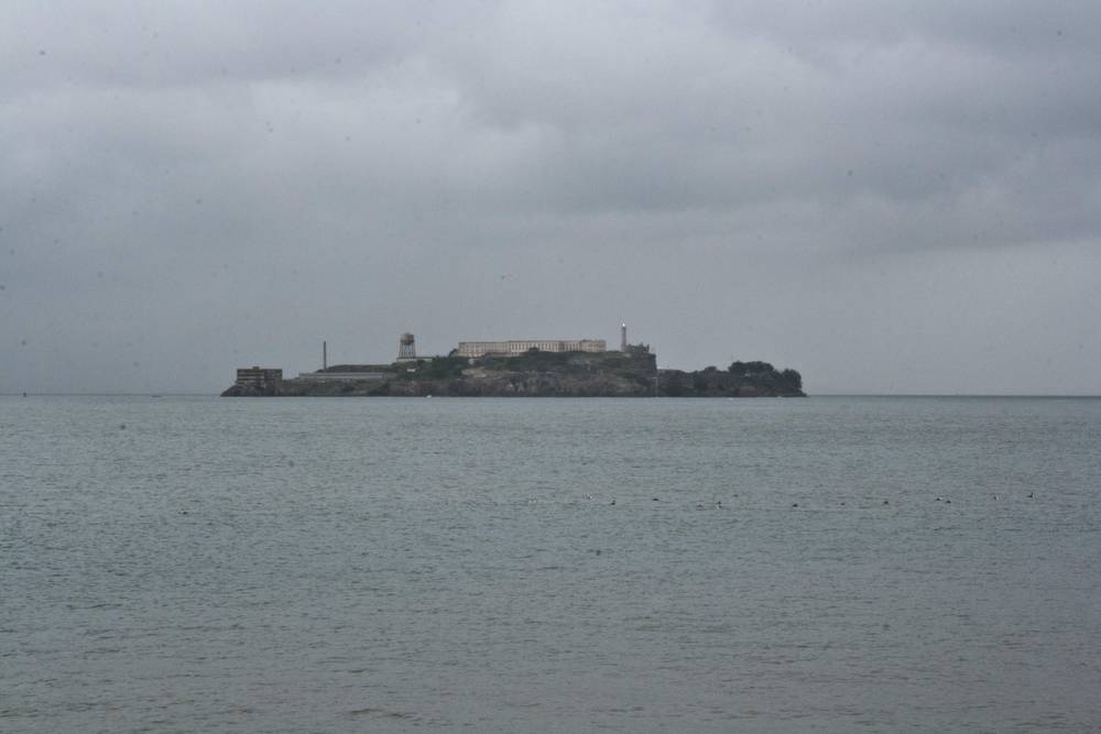 Alcatraz Island's buildings are seen clearly across calm gray water.