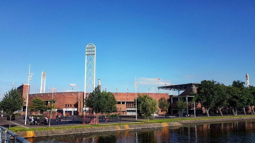 A red brick sports hall beside a canal under a clear blue sky.